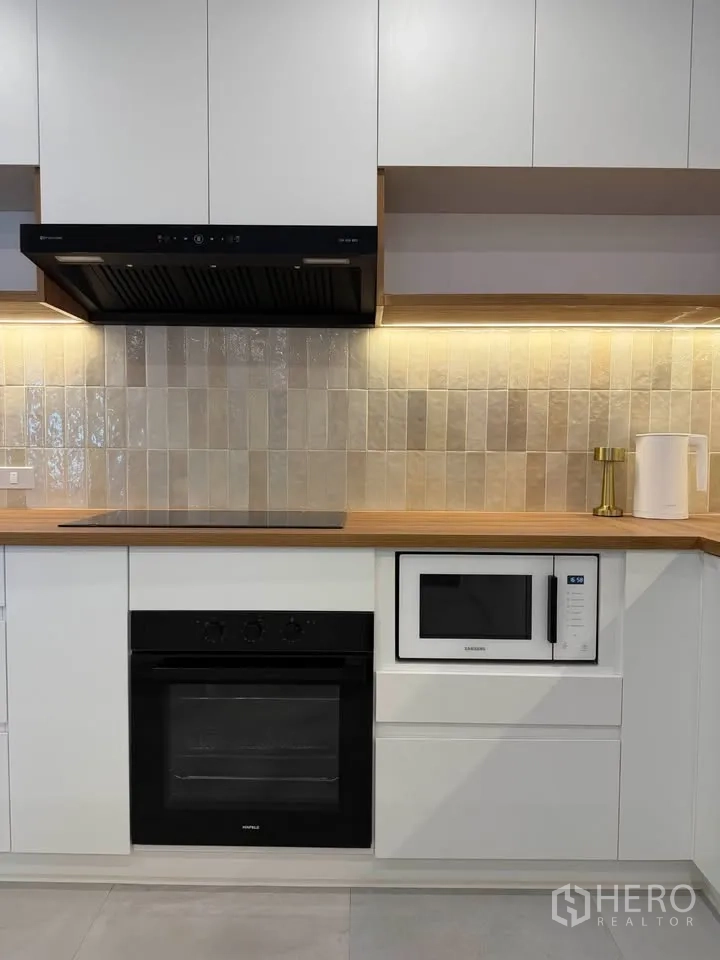 Condominium for rent in Watthana, Bangkok - Modern kitchen with oven, microwave, and tiled backsplash under lighting.