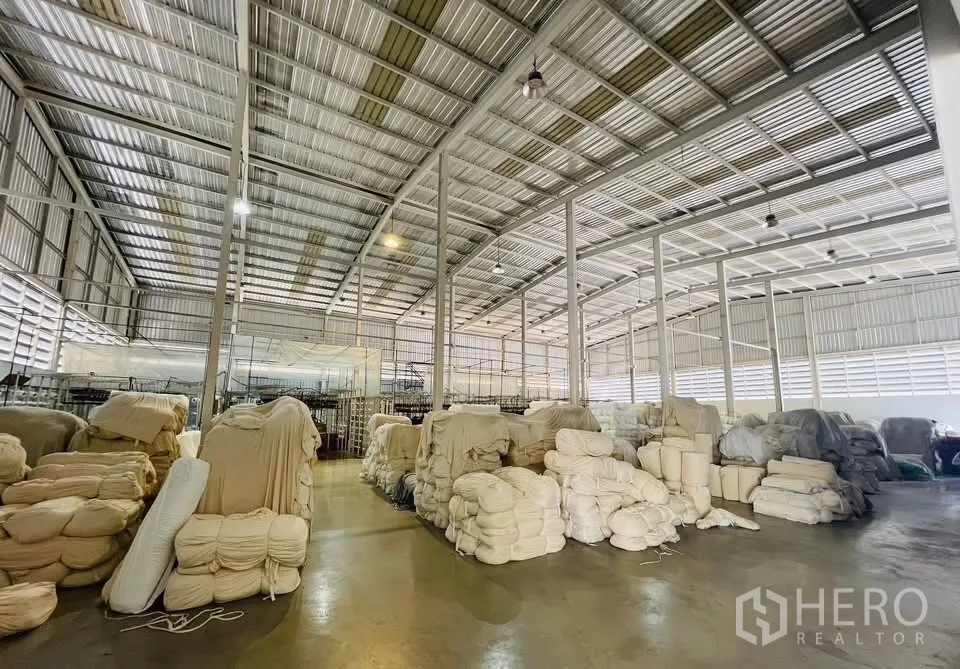 工厂 出售在Krathum Baen, Samut Sakhon - 仓库区域，堆放大量布料卷，金属屋顶通风良好