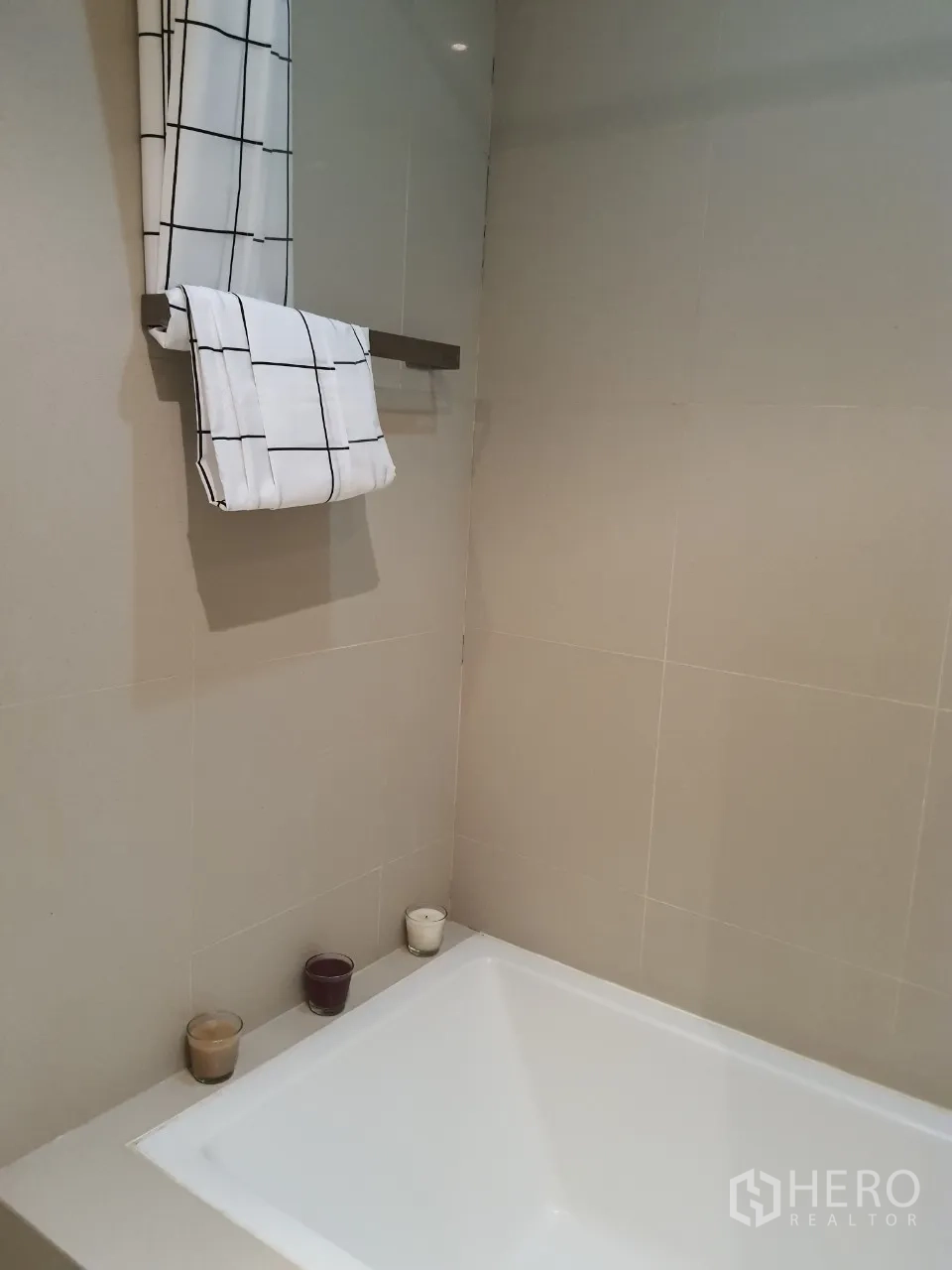 Condominium for rent or sale in Watthana, Bangkok - Modern bathroom featuring a built-in bathtub, beige tiles and a towel rack with patterned towels.