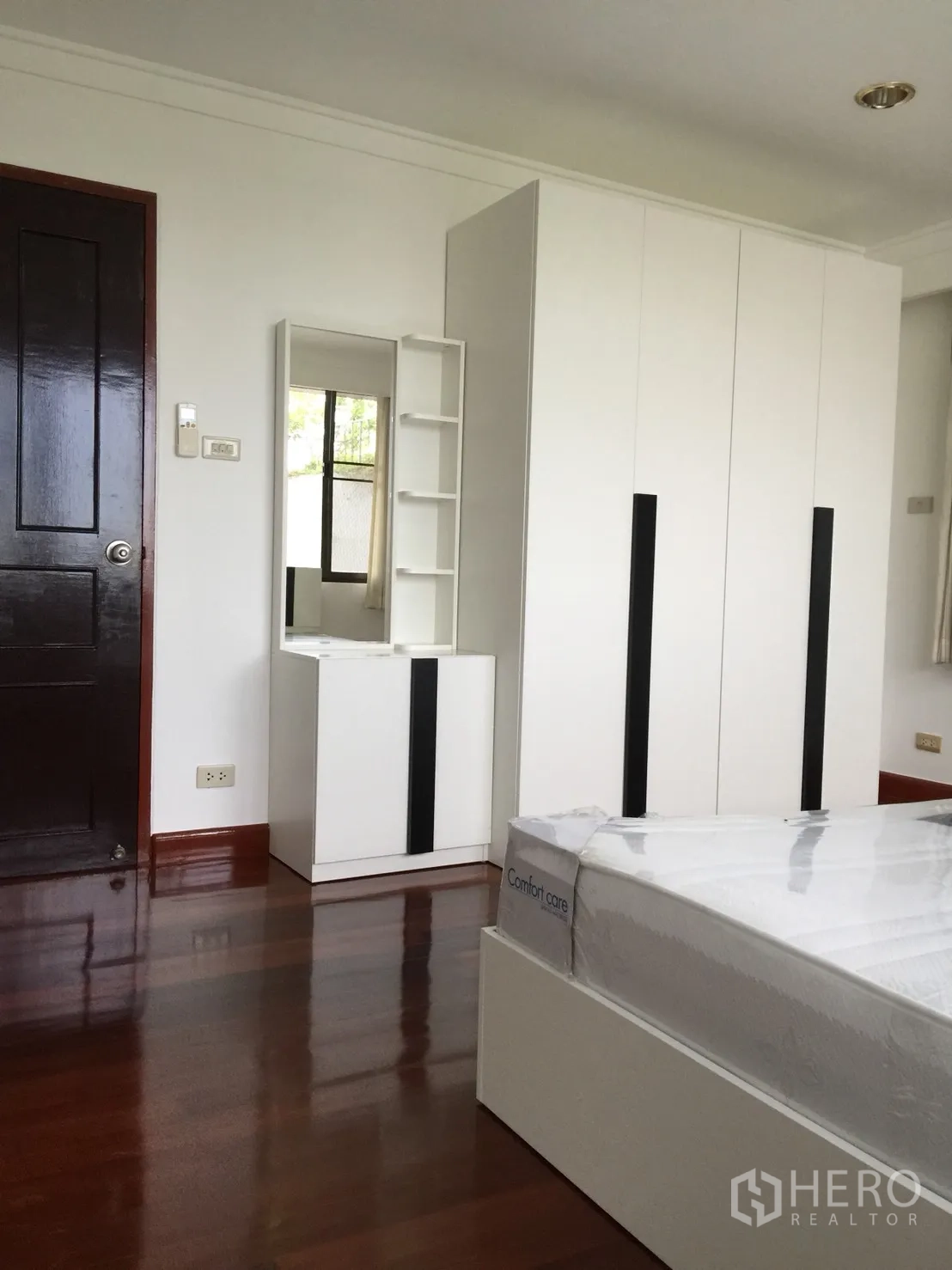Condominium for rent or sale in Watthana, Bangkok - Bedroom with white wardrobe, vanity unit and glossy wooden flooring.