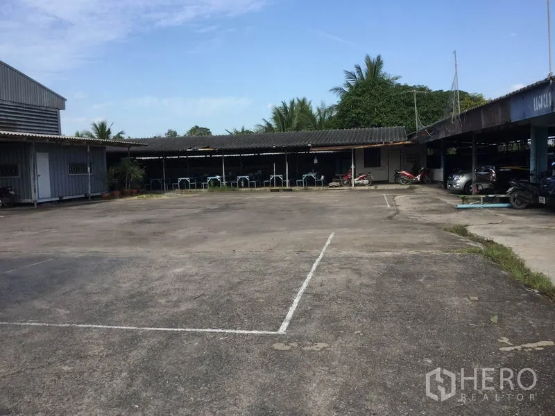 Warehouse for sale in Sai Noi, Nonthaburi - Expansive concrete yard with covered bays and parking beside the warehouse.