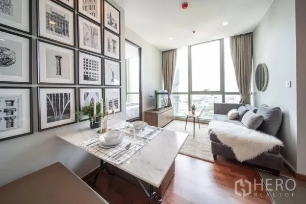 Condominium for rent in Ratchathewi, Bangkok - Bright living and dining area with marble table, gallery wall, wood floors, and floor-to-ceiling windows overlooking the city.