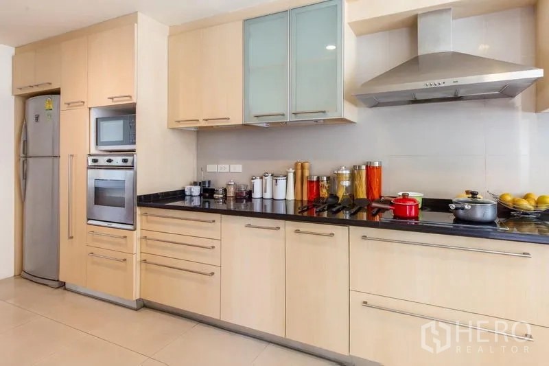 Condominium for rent in Bang Rak, Bangkok - Contemporary kitchen with light wood cabinetry, built-in oven, range hood and black stone countertops.