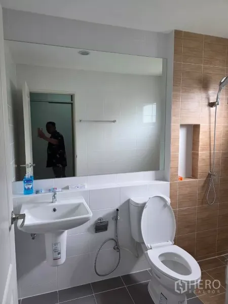 Detached House for rent in Bang Phli, Samut Prakan - Bathroom view showing large mirror, sink, toilet and a shower niche in a clean contemporary design.