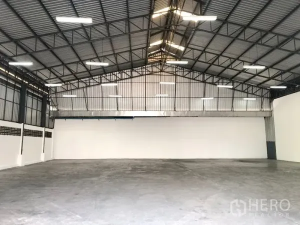 Warehouse for rent in Pak Kret, Nonthaburi - Clear-span warehouse floor with white walls, skylights, and ample ceiling lights for operations.