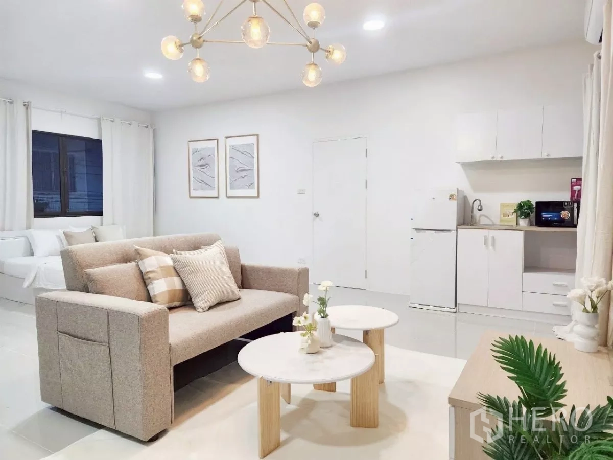 Detached House for rent in Chatuchak, Bangkok - Open-plan studio with sofa, coffee tables, kitchenette and bed in airy white decor.