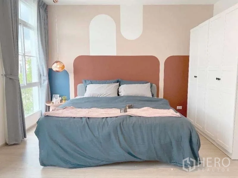 Townhouse for rent in Bang Bo, Samut Prakan - Sunlit master bedroom with geometric accent wall, large bed, bedside tables and a white wardrobe.