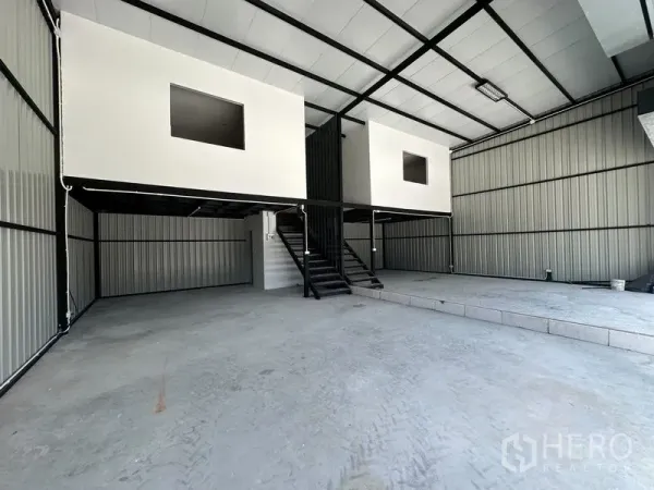 Warehouse for rent - Open storage bay with raised loading platform and twin mezzanine rooms in a metal-clad warehouse.