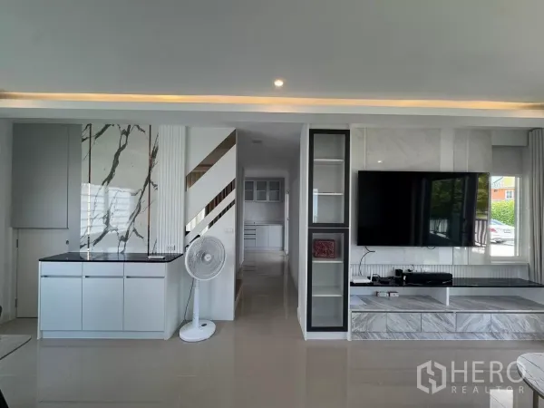 Detached House for rent in Bang Phli, Samut Prakan - Built-in media wall with large flat-screen TV and storage cabinetry looking toward the kitchen.