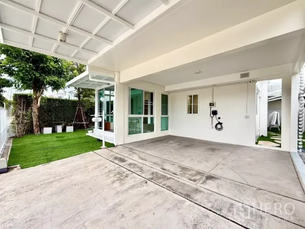 Detached House for rent in Bang Phli, Samut Prakan - Covered double carport with EV charger beside lawn and sliding glass doors.