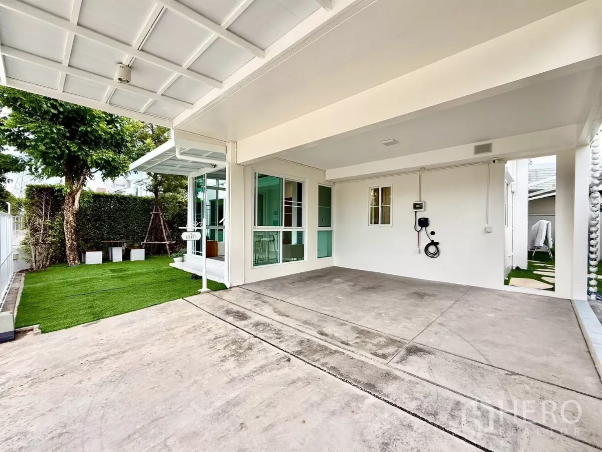 Detached House for rent in Bang Phli, Samut Prakan - Covered double carport with EV charger beside lawn and sliding glass doors.