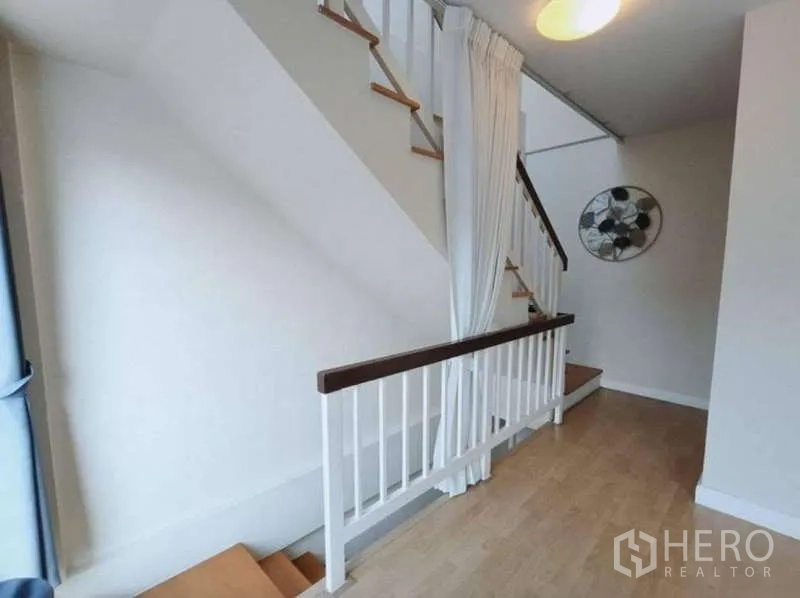 联排别墅 出租在Bang Kapi, Bangkok - 楼梯平台，白色扶手、布帘隔断与木质台阶。