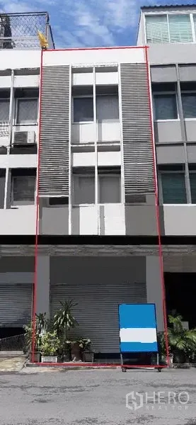 店屋 出租在Watthana, Bangkok - 现代多层店屋立面，底层卷帘门与竖向百叶，摆放盆栽的街景，通罗区域白天实景