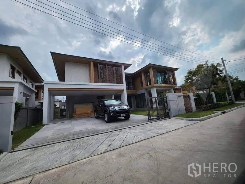 บ้าน ขายในSai Mai, Bangkok - มุมมองจากถนนของบ้านสองชั้นสมัยใหม่ พร้อมรั้ว ประตูทางเข้า และที่จอดรถภายในหมู่บ้านเงียบสงบ
