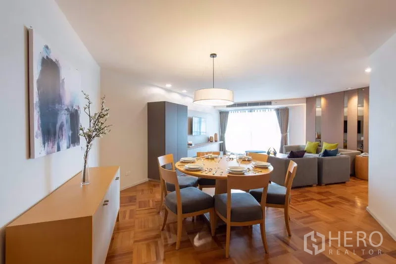Apartment for rent - Dining zone with a round six‑seat table under a pendant light, sideboard and view to a bright living room.