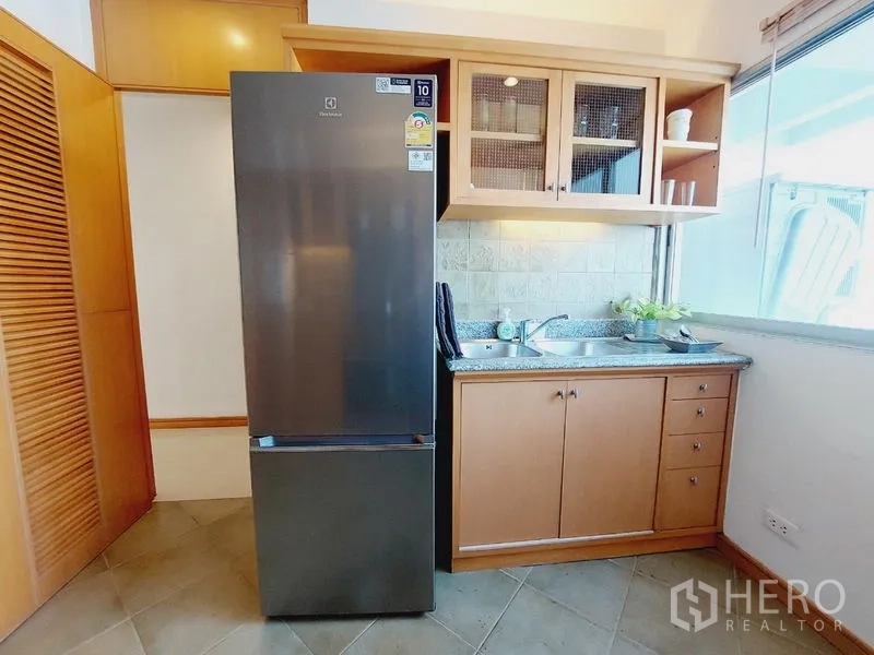 อพาร์ทเมนท์ ให้เช่า - มุมครัวมีตู้เย็นสูง อ่างล้างจาน ตู้กระจก และแสงธรรมชาติจากหน้าต่าง