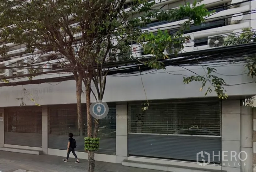 พื้นที่ขายปลีก ให้เช่าในPathum Wan, Bangkok - ด้านหน้าตึกชั้นล่างพร้อมประตูม้วนหน้ากว้าง กระจกบานใหญ่ และทางเท้ามีต้นไม้