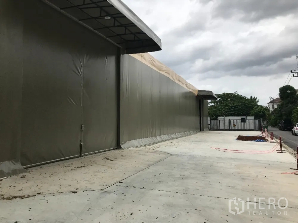 Warehouse for rent in Huai Khwang, Bangkok - Long warehouse exterior with canopy edge and wide concrete apron along a local road.