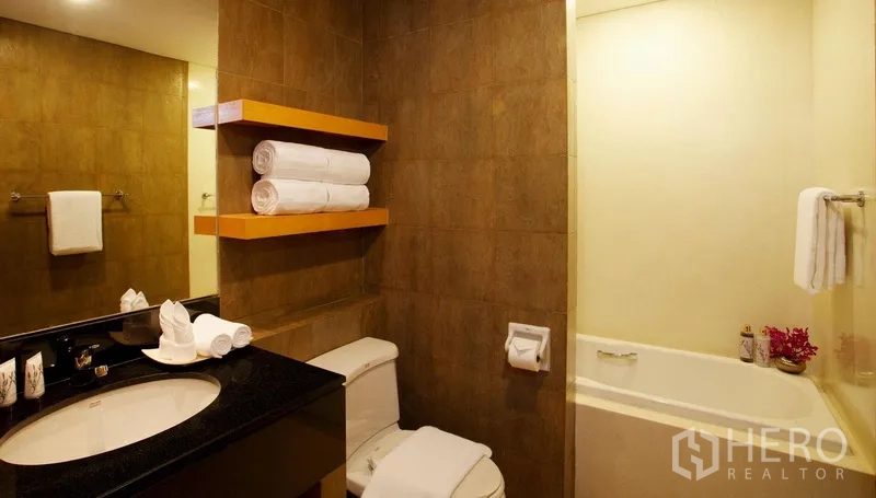Condominium for rent in Watthana, Bangkok - Warm-toned bathroom featuring a bathtub, vanity with black countertop and floating towel shelves.