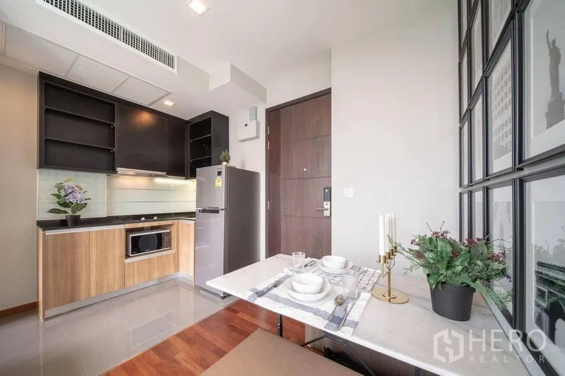 Condominium for rent in Ratchathewi, Bangkok - Compact modern kitchen with wood and black cabinetry, stainless refrigerator, and a two-seat dining nook.