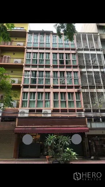 店屋 出租在Bang Rak, Bangkok - 席隆街道上的多层临街商铺外立面，落地窗、遮阳棚与盆栽。