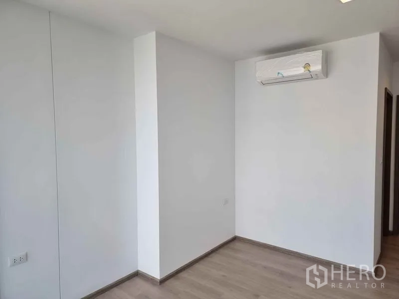 Condominium for sale in Phaya Thai, Bangkok - Second bedroom with white walls, wood floors and wall-mounted air conditioner.