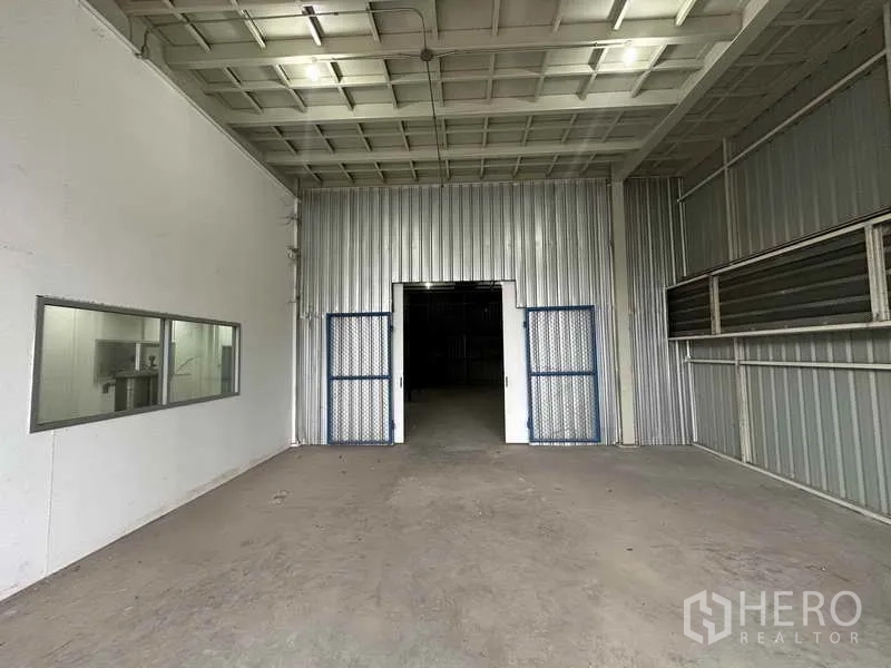 Home Office for rent in Bang Khen, Nonthaburi - Interior loading area with double steel doors and a viewing window into an adjacent room.