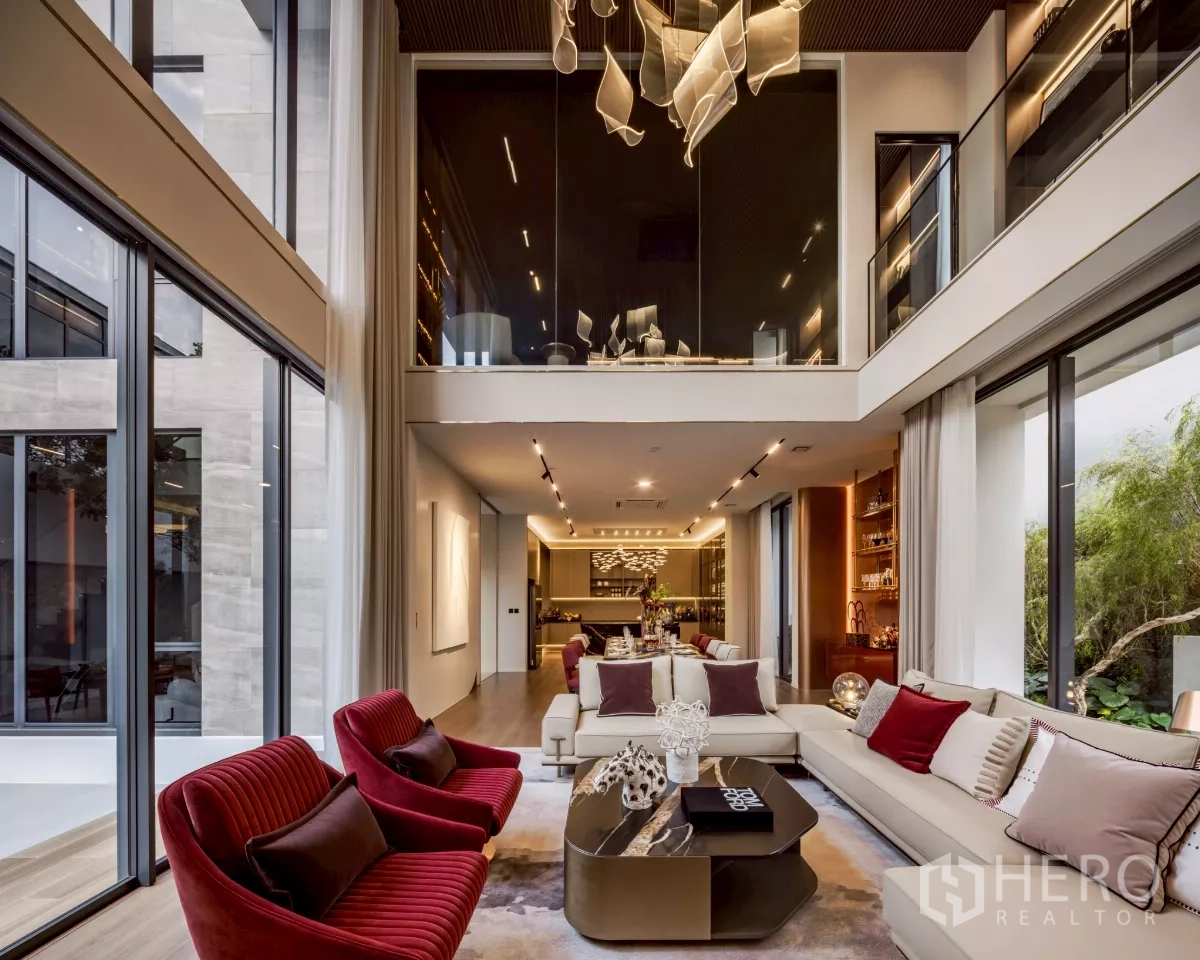 Detached House for rent in Saphan Sung, Bangkok - Double‑height living room opening to the kitchen with large glazing, plush sofas and sculptural chandelier.