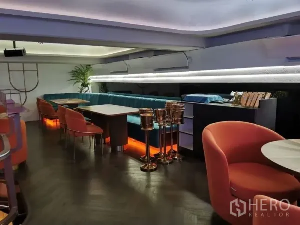 พื้นที่ขายปลีก ให้เช่า - มุมชั้นลอยพร้อมโซฟายาวสีเขียวไฟซ่อน เก้าอี้ส้ม และไฟตกแต่งสมัยใหม่