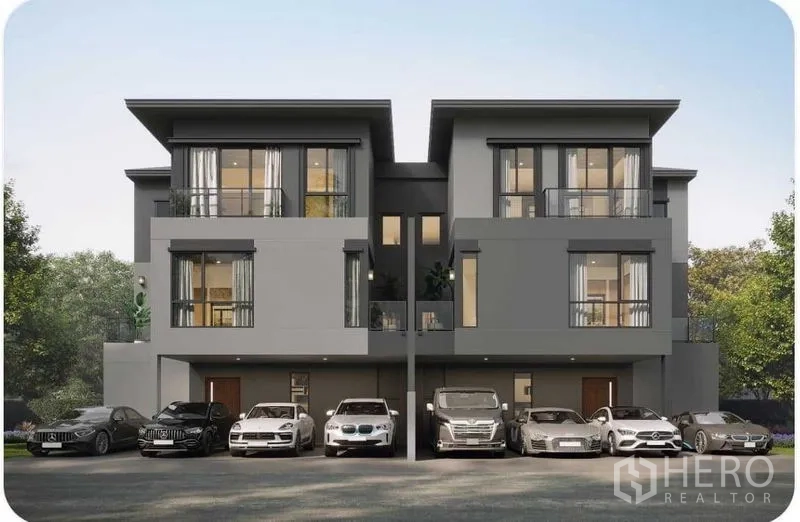 Detached House for sale in Prawet, Bangkok - Contemporary three-storey houses with wide balconies and floor-to-ceiling windows, with multiple cars parked along the front.