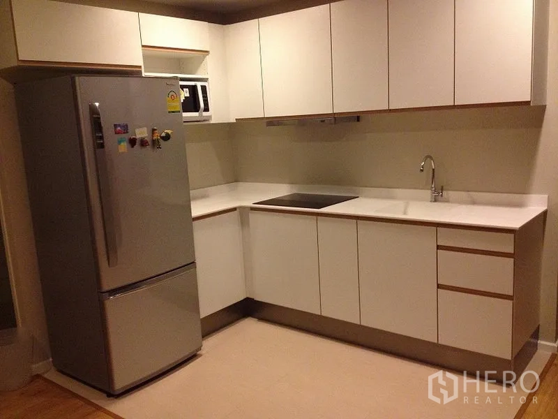 公寓 出租在Pathum Wan, Bangkok - 现代L形厨房，白色柜体，电磁炉、微波炉与不锈钢冰箱。