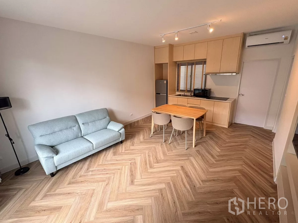 Townhouse for rent in Bang Phli, Samut Prakan - Open-plan living area with sofa, dining set and light-wood kitchenette on herringbone flooring.