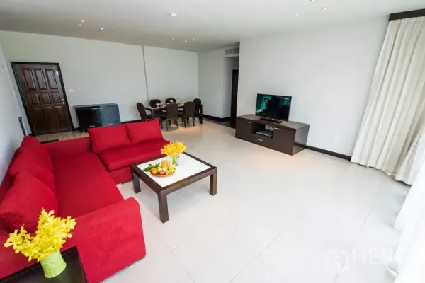 Apartment for rent in Sathon, Bangkok - Spacious open-plan living room with red sectional sofa, TV unit, and dining area by wide windows.