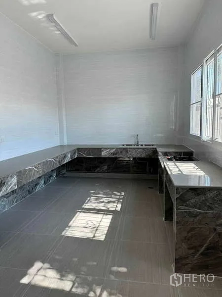Detached House for rent in Samut Prakan - Bright kitchen with L-shaped stone countertops, tiled floor, and large windows.