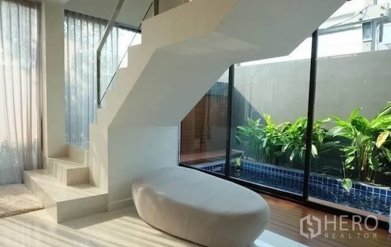 Townhouse for rent in Watthana, Bangkok - Stair landing facing a private plunge pool and greenery through a glass wall.