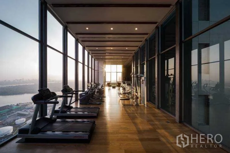 Condominium for rent or sale in Bang Rak, Bangkok - High-rise fitness room with treadmills and panoramic river and city skyline views through floor-to-ceiling glass.