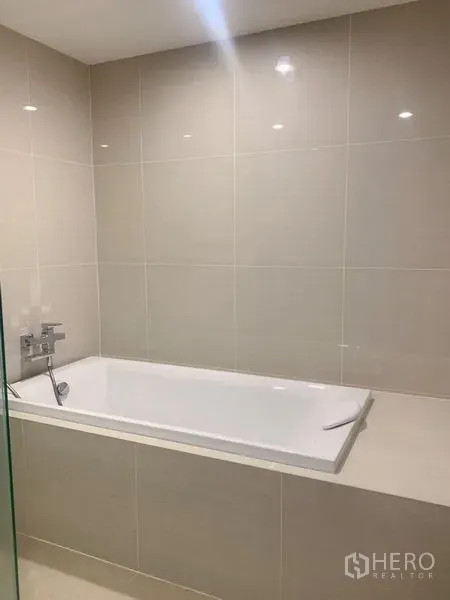 Condominium for sale in Bang Na, Bangkok - Built-in bathtub with beige tiled walls and chrome faucet in a modern bathroom.