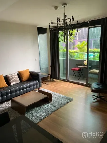 คอนโด ให้เช่าในKhlong Toei, Bangkok - ห้องนั่งเล่นติดประตูกระจกบานเลื่อนเต็มผนัง เปิดสู่ระเบียง วิวสระว่ายน้ำและสวน พร้อมโซฟาหนังและม่านทึบ