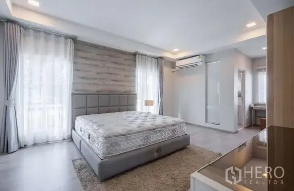 Detached House for rent in Prawet, Bangkok - Bright master bedroom with large windows, upholstered bed, air conditioner and wood accent wall.