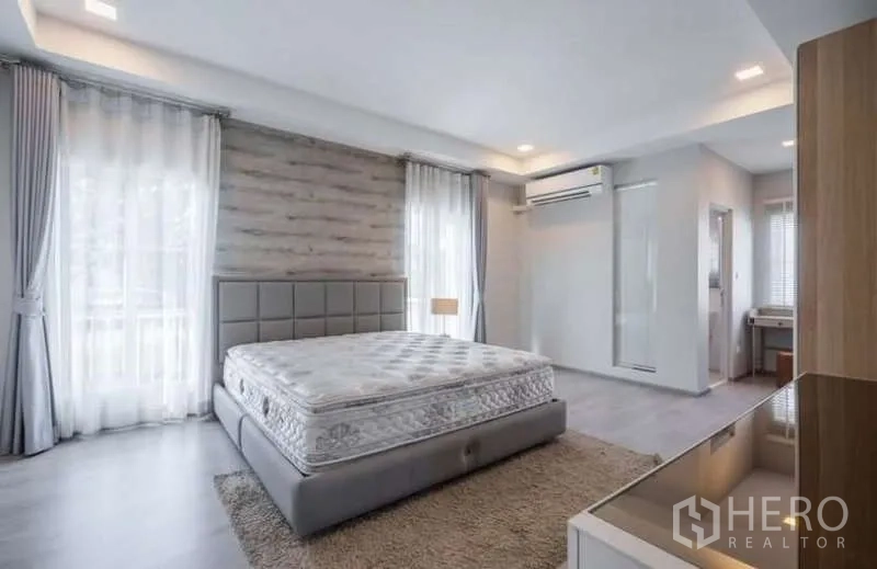 Detached House for rent in Prawet, Bangkok - Bright master bedroom with large windows, upholstered bed, air conditioner and wood accent wall.