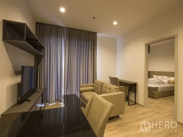 Condominium for rent in Chatuchak, Bangkok - Living space facing tall curtains with sofa, work desk, and doorway to the bedroom.