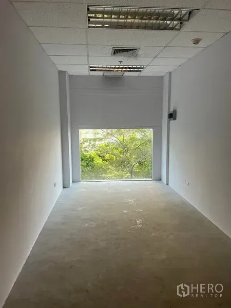 零售空间 出租在Bang Rak, Bangkok - 狭长白色铺位，尽端大窗可见绿树，吊顶照明与水泥地面。