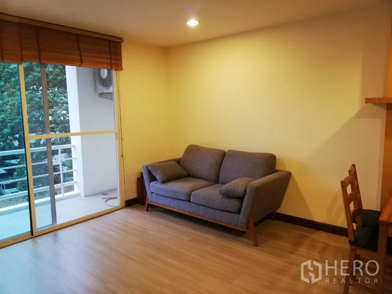 Condominium for rent in Watthana, Bangkok - Cozy living room with gray sofa opening to a balcony overlooking greenery.