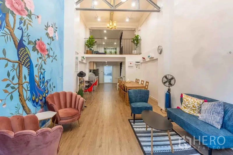 Townhouse for rent in Bang Rak, Bangkok - Bright double-height living area with mezzanine, peacock mural, and mixed lounge seating.