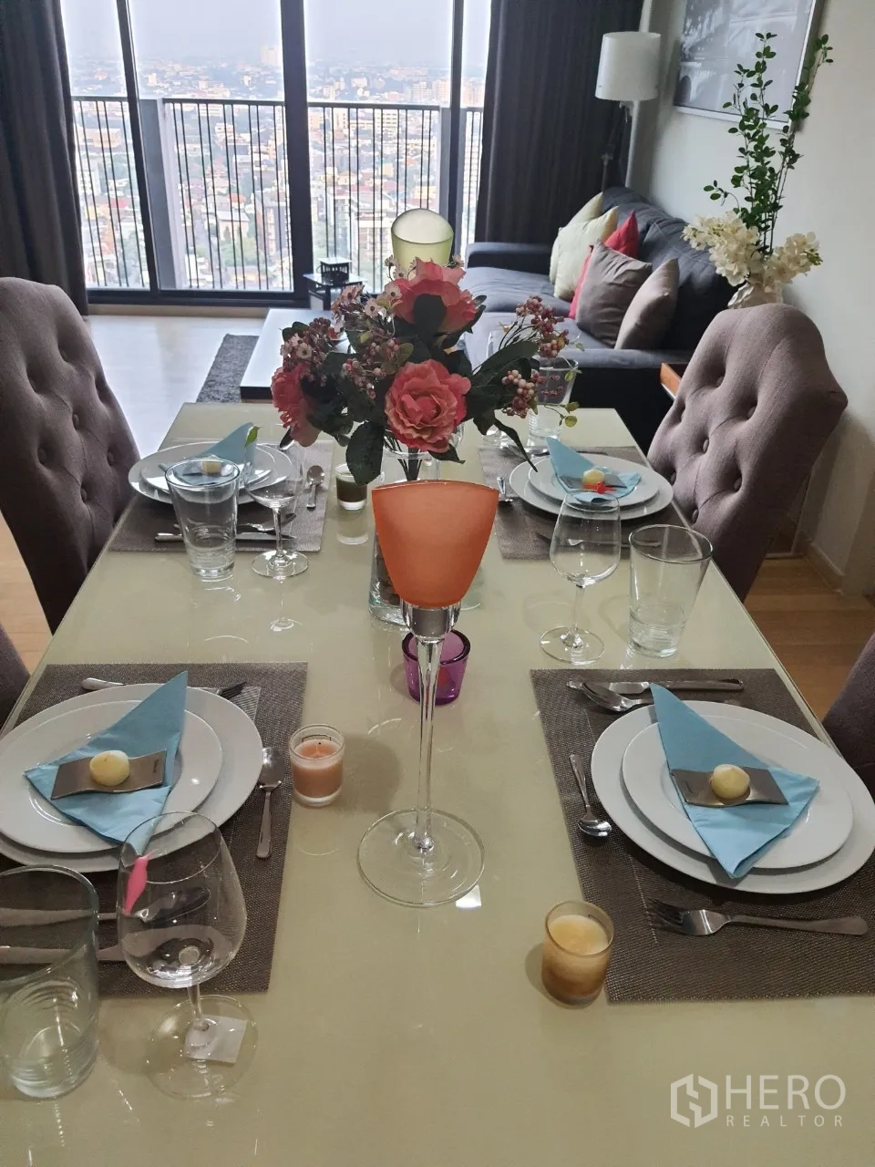 Condominium for rent or sale in Watthana, Bangkok - Dining table set for four with glassware and flowers, opening to living room and city-view balcony.