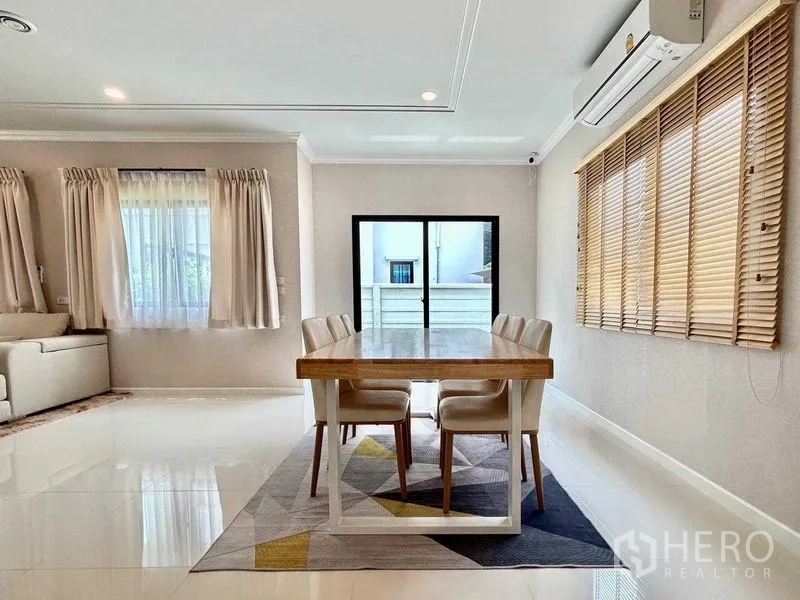 Detached House for rent in Khlong Sam Wa, Bangkok - Dining area with four-seat wooden table, wide window blinds and patio doors