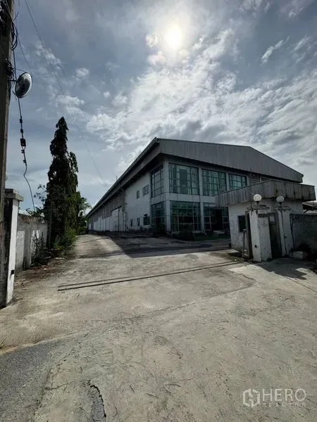 คลังสินค้า ให้เช่าในBang Phli, Samut Prakan - ด้านหน้าโกดังอุตสาหกรรมพร้อมถนนคอนกรีตกว้างและหลังคาเมทัลชีท ภายใต้ท้องฟ้าโปร่งในบางพลี