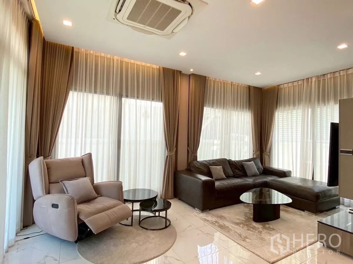 Detached House for rent in Bang Phli, Samut Prakan - Bright lounge with floor-to-ceiling curtains, a reclining armchair, sectional sofa and ceiling cassette air-conditioner.