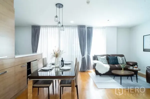 Condominium for sale in Watthana, Bangkok - Open-plan living and dining with pendant lights, leather sofa and wooden floor.