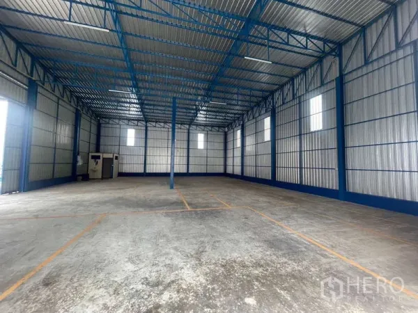 Warehouse for rent in Wang Thonglang, Bangkok - Spacious high-clear warehouse interior with blue steel trusses, concrete floor, and natural light windows.